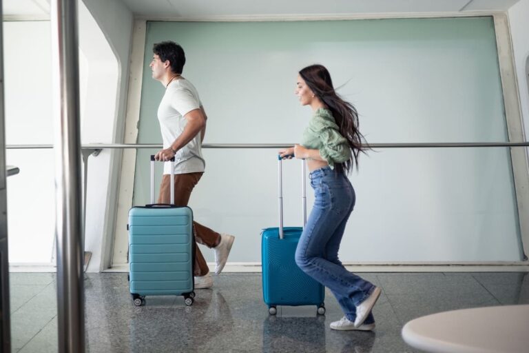 Multicultural couple running through an airport terminal with luggage after nearly missing their international flight