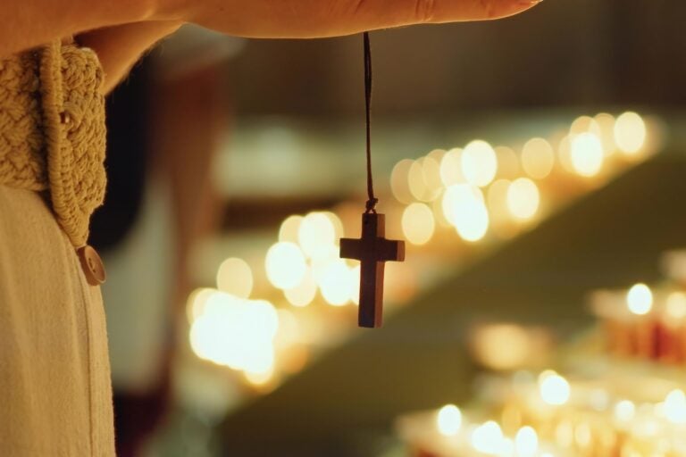 Woman with cross prays next to burning candles in church.