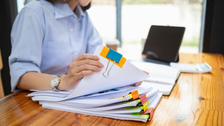 Person searching through a pile of important documents on a desk, illustrating the need to back up travel paperwork.