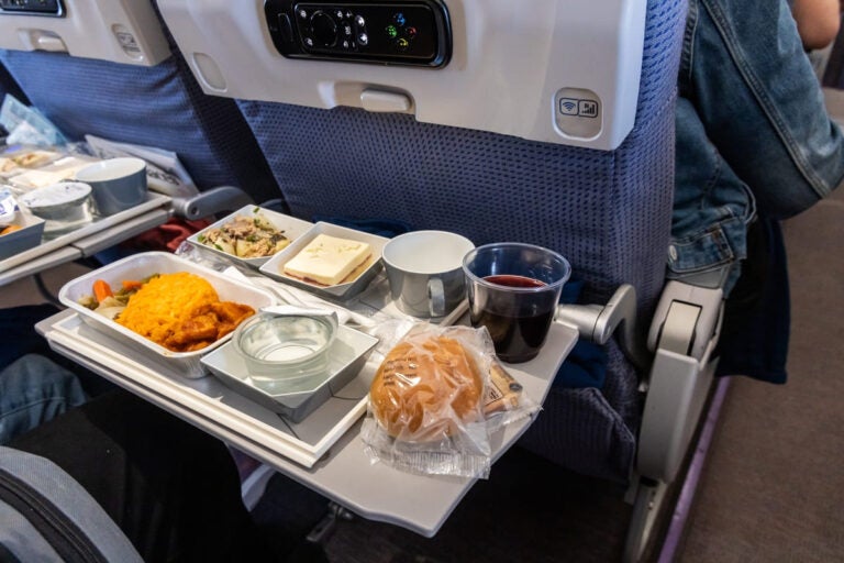 Inflight Asian meal set with rice spicy chicken dessert bun and red wine served on airplane tray