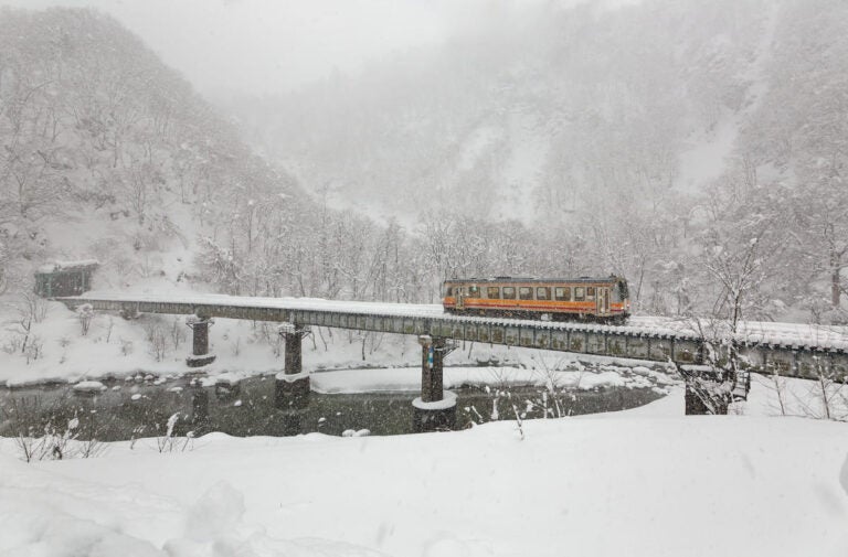 Local train crossing a snowy bridge in Japan, representing the importance of understanding transportation options while traveling.