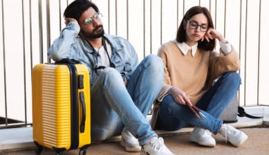 Stressed young couple holding passports and tickets at the airport, appearing worried about travel problems or missed flights.