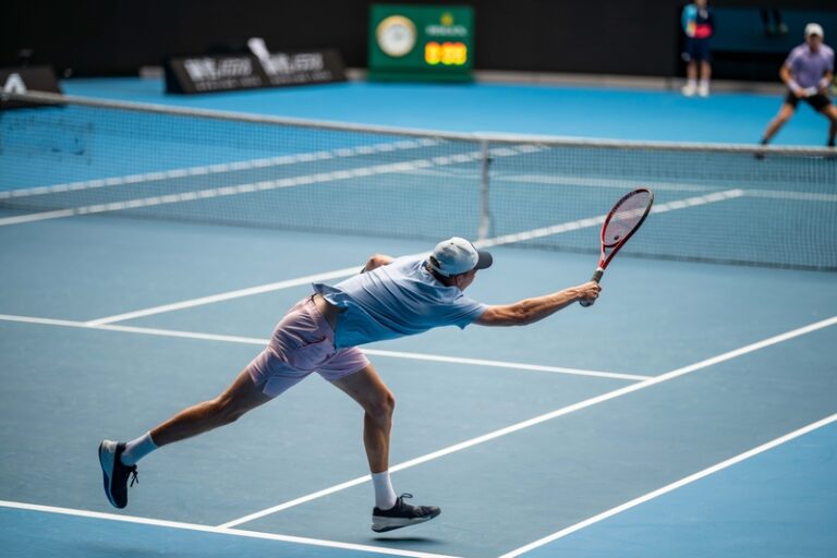Tennis player stretching to return the ball during a match on a hard court.