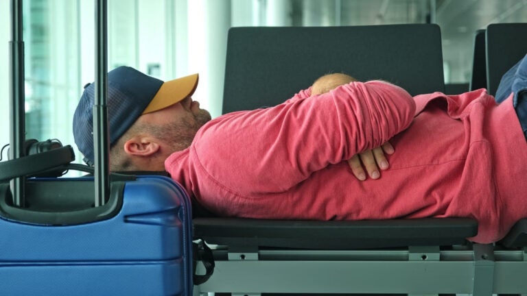 Tired passenger experiencing jet lag resting on a bench at an airport terminal departure hall