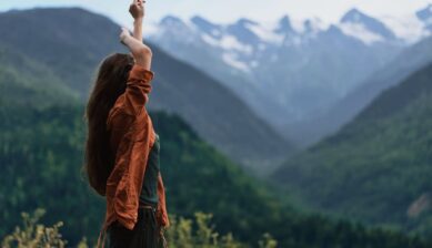 Woman standing in the mountains with her arms raised, expressing freedom and calm authenticity in a peaceful outdoor landscape.