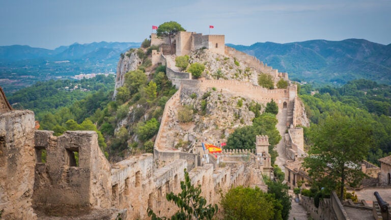 Xàtiva Castle stretching across a rocky hill surrounded by green mountains.