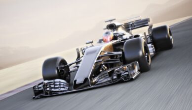 A silver and black Formula 1 race car speeding along a race track, with motion blur on the wheels and background suggesting high velocity, set against a hazy desert landscape.