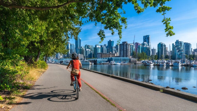 Woman cycling along the Stanley Park seawall with Vancouver's cityscape in the background on a summer day