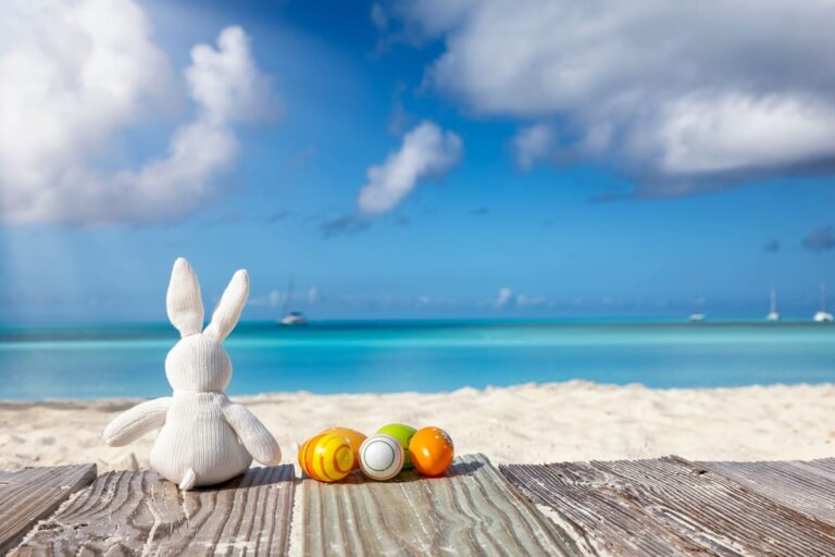 Easter travel concept with a white bunny and colorful eggs on a tropical beach