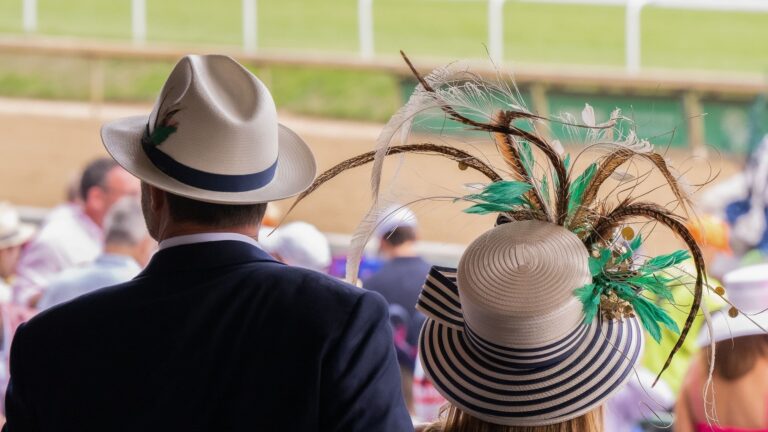 Racegoers wearing elegant hats and formal attire at a horse racing event