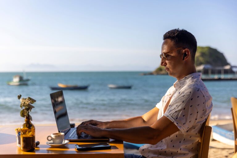 man on his laptop sitting in a cafe by the beach