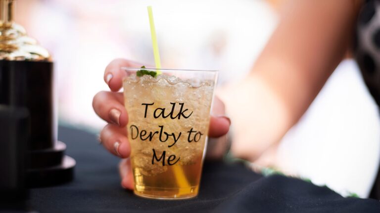 A hand holding a classic mint julep cocktail in a silver cup at a Kentucky Derby party