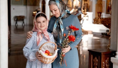 Mother and daughter holding Easter eggs and praying together in an Orthodox church on Easter