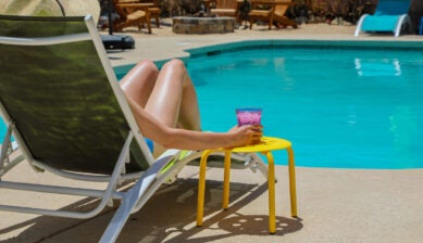 Woman relaxing poolside in a straw hat with a pink drink during a sunny day in Palm Springs