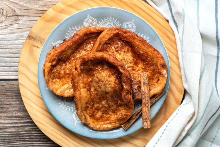 Plate of traditional Spanish torrijas with cinnamon stick on a wooden table for Easter