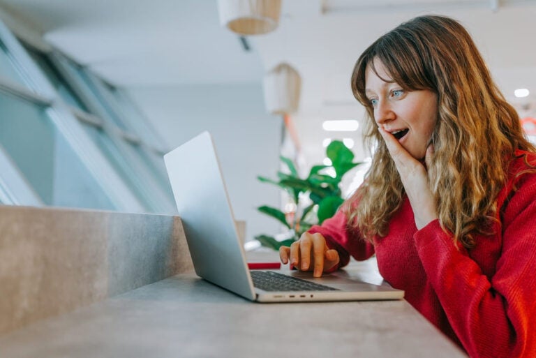 Smiling woman in red sweater looking up affordable Asia flight deals on a laptop