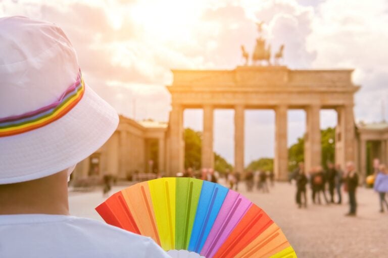 Woman in Berlin with rainbow fan and ribbon on white summer hat,