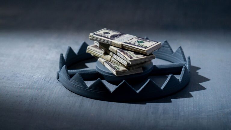 A stack of US dollar bills resting inside the jaws of a metal bear trap, symbolizing financial risk.