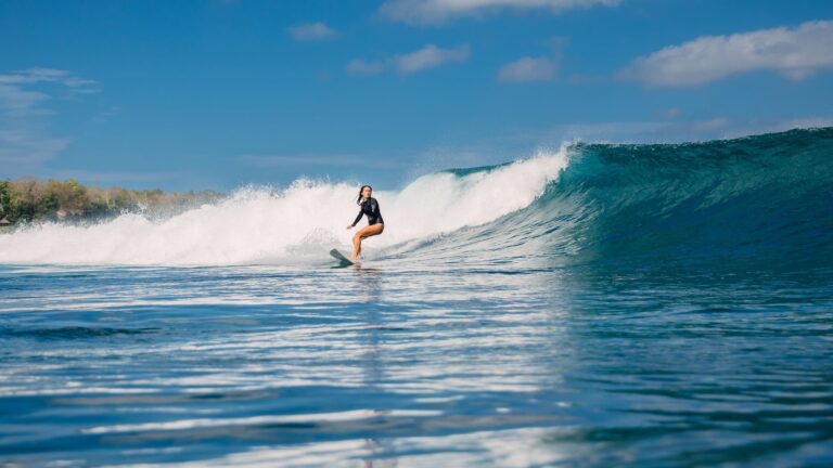 Female surfer riding a clean blue wave on a sunny day in Bali