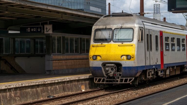 A yellow and grey Belgian train waiting at a covered station platform