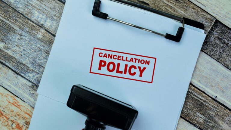 A red-handled rubber stamper resting on a wooden table next to the words "Cancellation Policy," illustrating the concept of booking terms and conditions.
