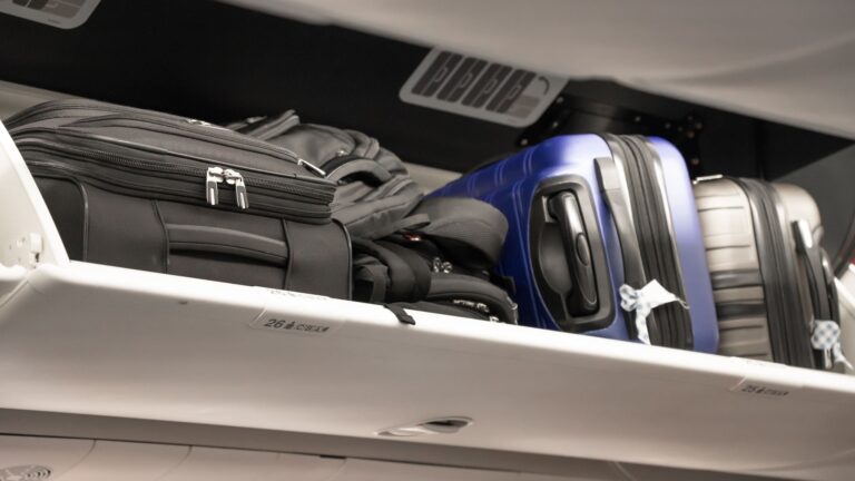 Rows of carry-on luggage stored in open overhead compartments inside a commercial passenger aircraft cabin.