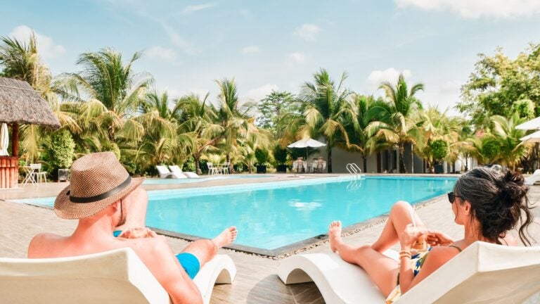 Couple relaxing on sunbeds at a tropical all-inclusive resort with a swimming pool and palm trees