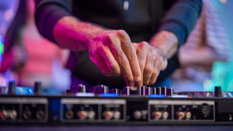 Close-up of a male DJ mixing music on a controller under neon lighting at an electronic music party.