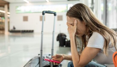 A weary female traveler sitting beside her luggage at an international airport terminal after a flight cancellation.