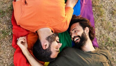 A smiling couple holds a rainbow Pride flag together, celebrating their identity as part of the LGBTQ+ community.