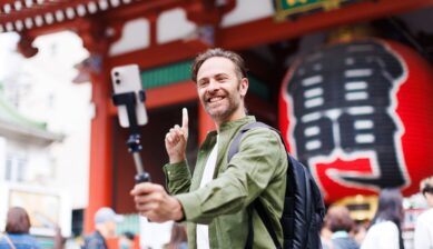 A Caucasian man smiling and taking a selfie with his mobile phone while visiting Japan.