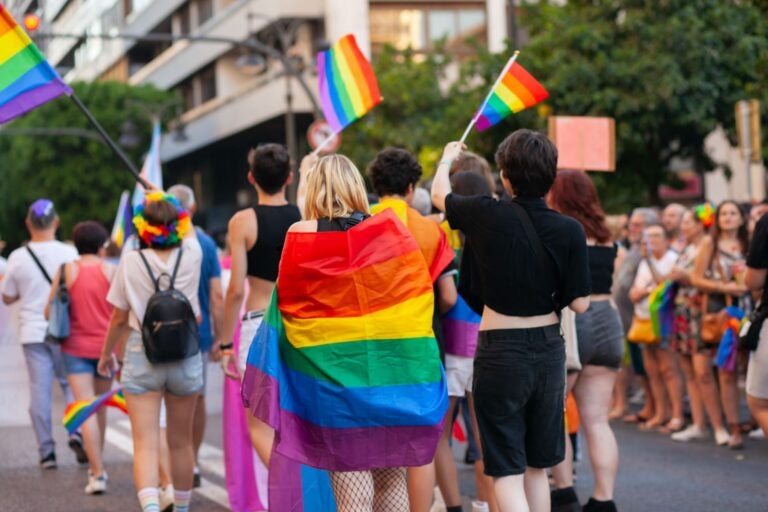 People walking at Pride parade with rainbow flag.