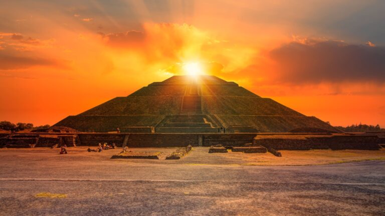 The ancient pyramid complex at Teotihuacán bathed in warm sunset light, with the Pyramid of the Sun visible against a hazy sky over the Valley of Mexico.