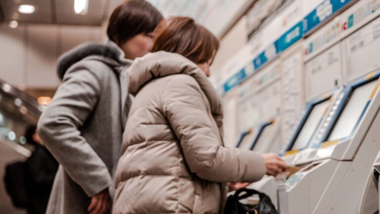 A blurred passenger standing at a self-service ticket machine inside Osaka train station.