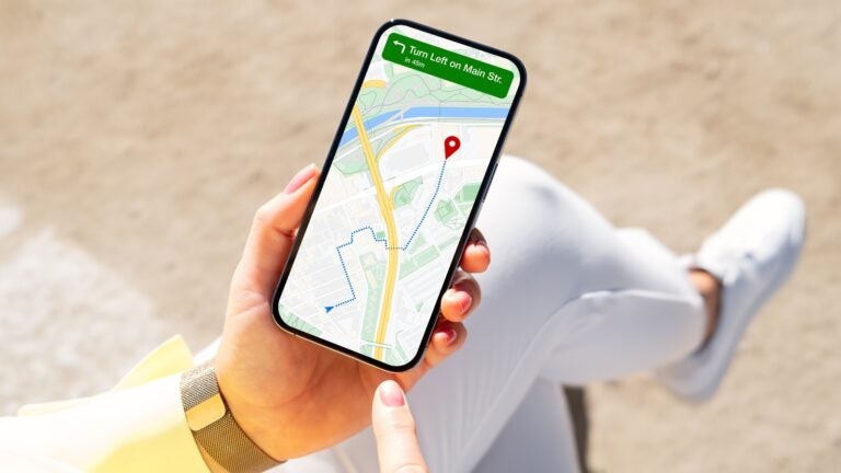 A person standing on a city street, holding a smartphone displaying a map navigation app with route directions.