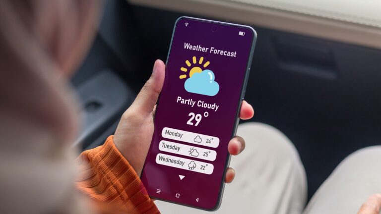 A Muslim woman sitting in a car looking at a weather forecast app on her smartphone before a trip.
