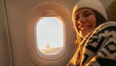 A young woman gazing out of an airplane window bathed in warm golden hour light during a flight.
