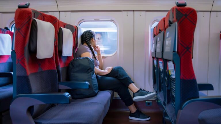 A young woman sitting by the window of a Japanese high-speed train, with a travel backpack beside her.