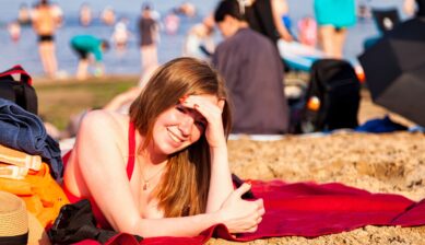 Young woman in a red swimsuit relaxing on a sandy beach in Jūrmala, Latvia, with swimmers visible in the background