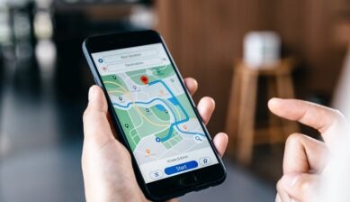A young woman's hand holding a smartphone and browsing a map or location search app while on the go.