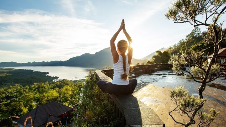 Woman practicing yoga on a hilltop at sunrise with a volcano in the background in Bali, Indonesia
