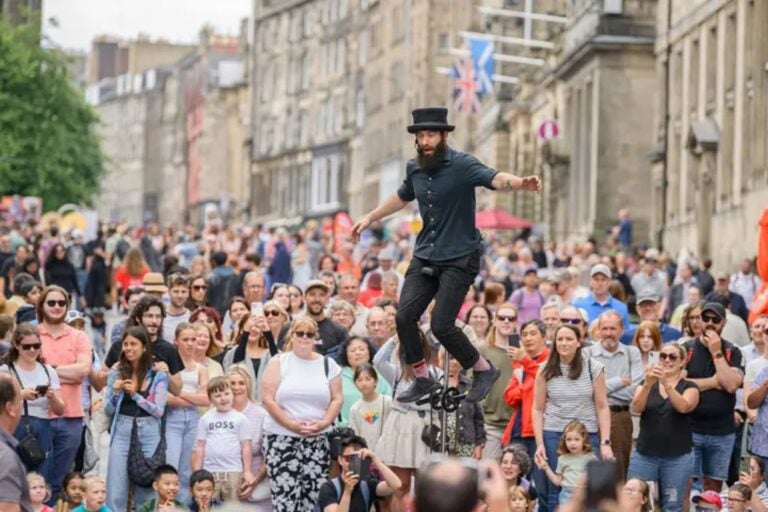 A street performer balancing on a unicycle above a large crowd on the Royal Mile, Edinburgh.