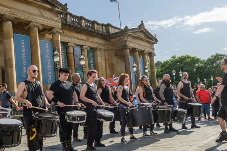 A line of drummers performing on snare drums outside the Scottish National Gallery.