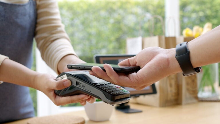 A small business owner in a coffee shop using a QR code scanner to process a contactless mobile payment from a customer.