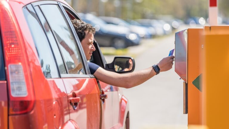 A hand tapping a credit card at a parking payment machine to pay for a parking space.