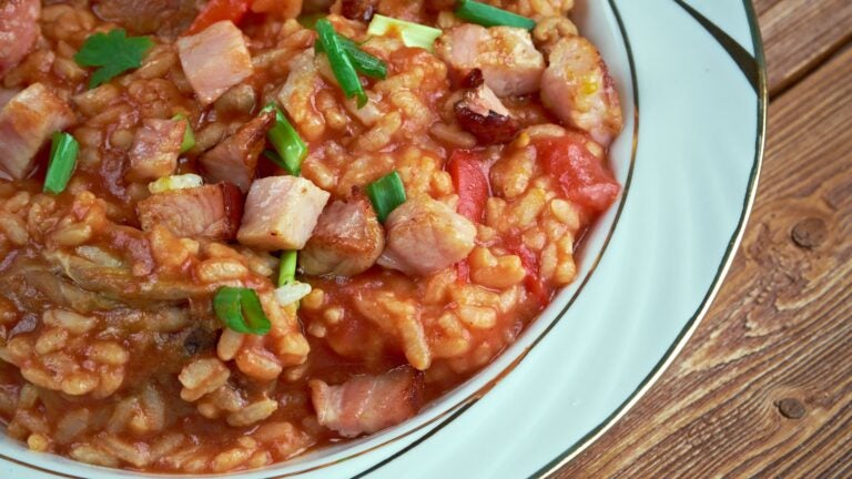 A skillet of Lowcountry red rice cooked with tomatoes, bacon, and sliced pork sausage, a staple dish of South Carolina's coastal cuisine.