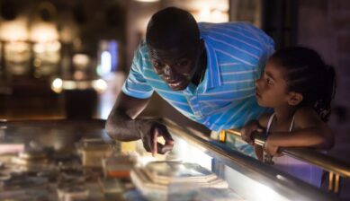 An African American father and daughter looking together at exhibits inside a historical museum.