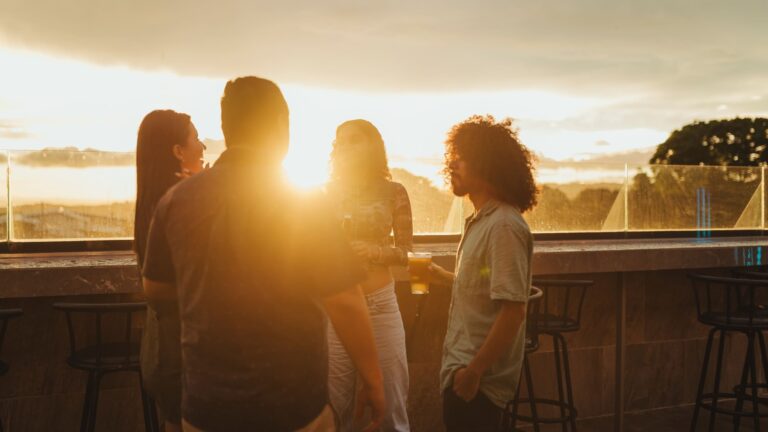 A group of friends in conversation at an outdoor rooftop bar during golden hour, with warm light and a relaxed social atmosphere.