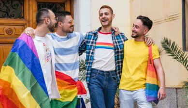 Four joyful friends celebrating together at a Pride event, holding rainbow flags and wearing LGBTQ Pride-themed accessories and clothing.