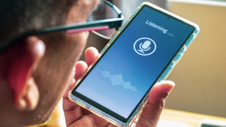 A South Asian man holding a smartphone close to his face while using a voice translation mobile app.